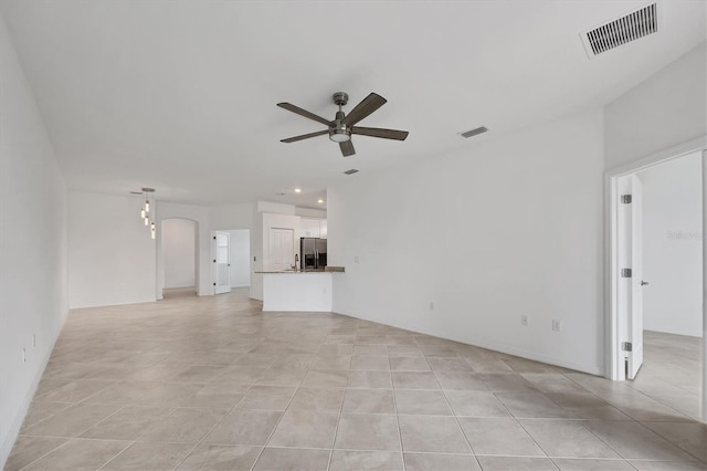 unfurnished living room featuring light tile patterned floors, ceiling fan, visible vents, and arched walkways