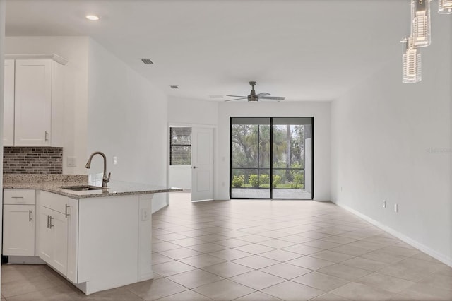 kitchen featuring visible vents, white cabinets, light stone counters, open floor plan, and a sink