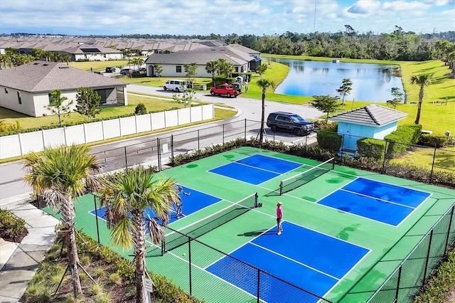 view of tennis court with a water view, a residential view, and fence