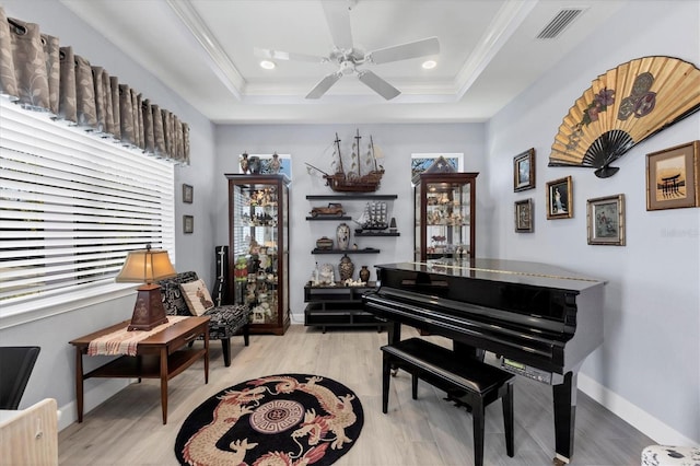 living area with light wood-style flooring, visible vents, a raised ceiling, and ornamental molding