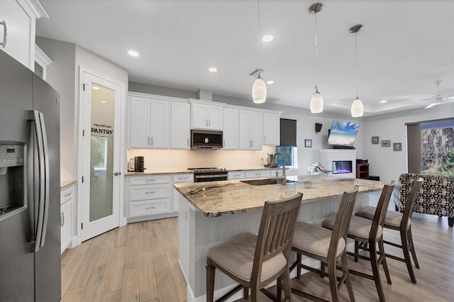 kitchen featuring tasteful backsplash, appliances with stainless steel finishes, light stone counters, light wood-type flooring, and a sink