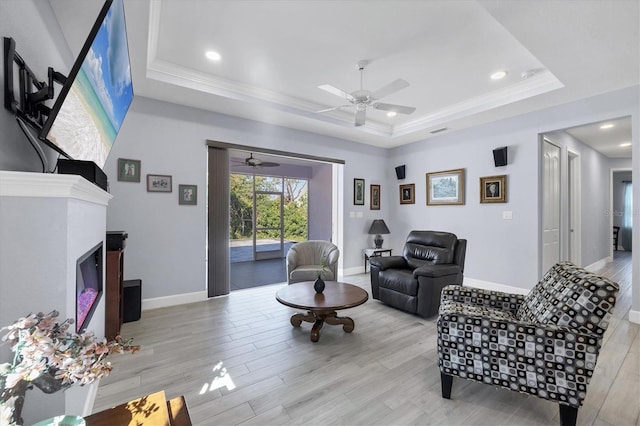 living area with baseboards, a tray ceiling, wood finished floors, and a glass covered fireplace