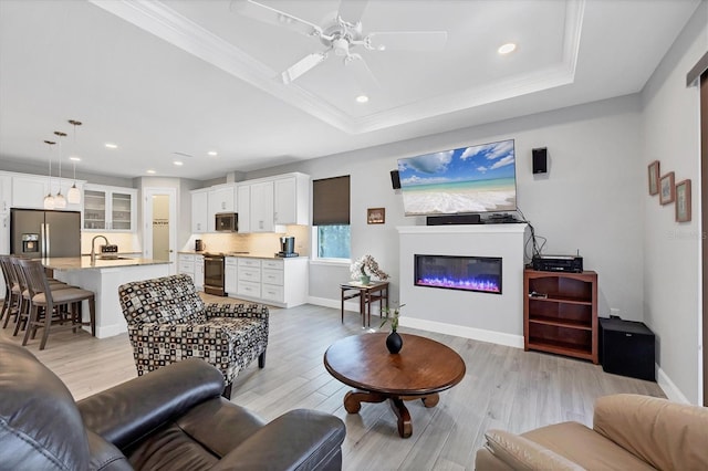 living room featuring light wood-style floors, baseboards, a raised ceiling, and a glass covered fireplace