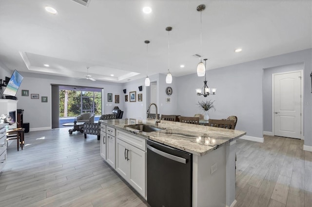 kitchen featuring a raised ceiling, light wood-style flooring, open floor plan, a sink, and dishwashing machine