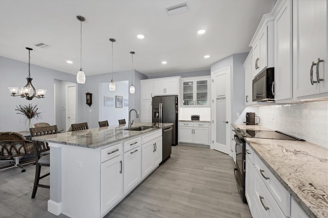 kitchen featuring visible vents, white cabinets, a kitchen breakfast bar, black appliances, and tasteful backsplash