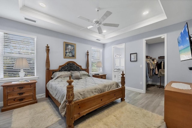 bedroom with baseboards, a raised ceiling, light wood-style flooring, ornamental molding, and a walk in closet