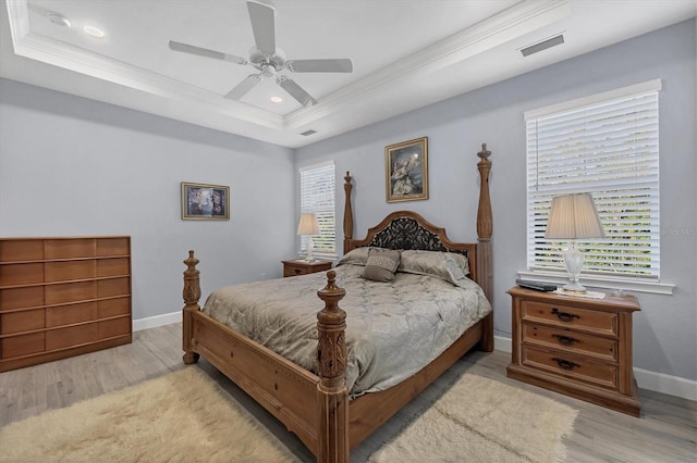 bedroom with a tray ceiling, visible vents, crown molding, and multiple windows