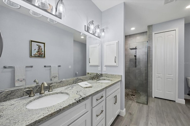 bathroom featuring double vanity, wood finished floors, a stall shower, and a sink