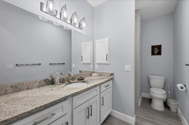 bathroom featuring toilet, baseboards, wood finished floors, and vanity