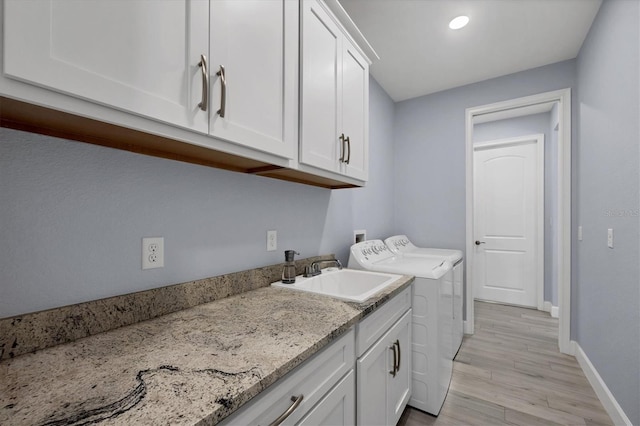 clothes washing area featuring washing machine and dryer, a sink, baseboards, cabinet space, and light wood finished floors