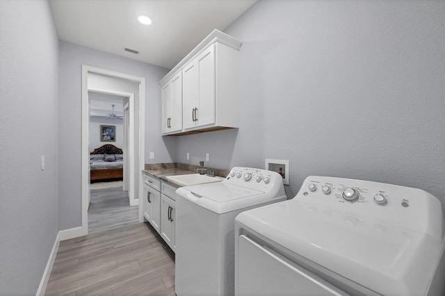 washroom with a sink, visible vents, light wood-style floors, independent washer and dryer, and cabinet space