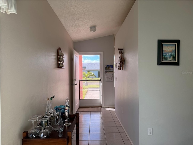 doorway featuring lofted ceiling, a textured ceiling, baseboards, and light tile patterned floors