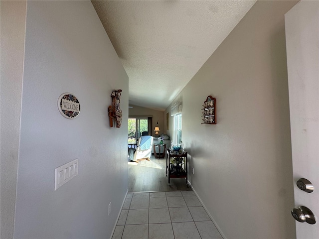 corridor with baseboards, vaulted ceiling, a textured ceiling, and light tile patterned flooring