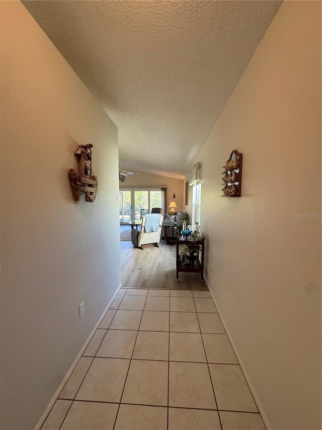 hallway featuring vaulted ceiling, a textured ceiling, light tile patterned flooring, and baseboards