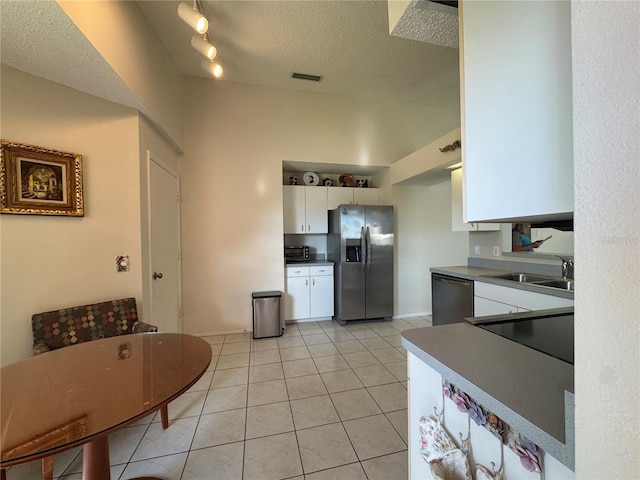 kitchen with light tile patterned floors, stainless steel appliances, a sink, white cabinets, and dark countertops