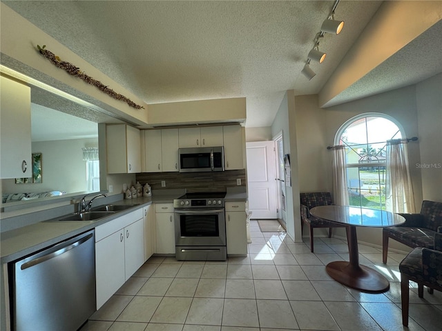 kitchen with light tile patterned floors, decorative backsplash, stainless steel appliances, a textured ceiling, and a sink