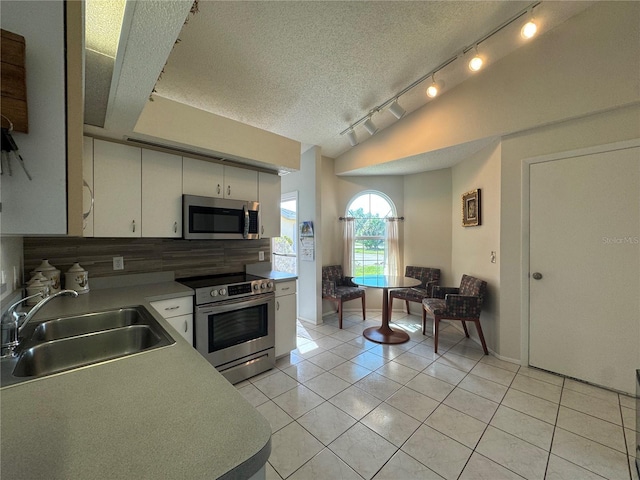 kitchen featuring light tile patterned floors, a sink, white cabinets, vaulted ceiling, and appliances with stainless steel finishes