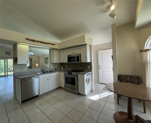 kitchen with light tile patterned floors, a sink, white cabinetry, appliances with stainless steel finishes, and decorative light fixtures