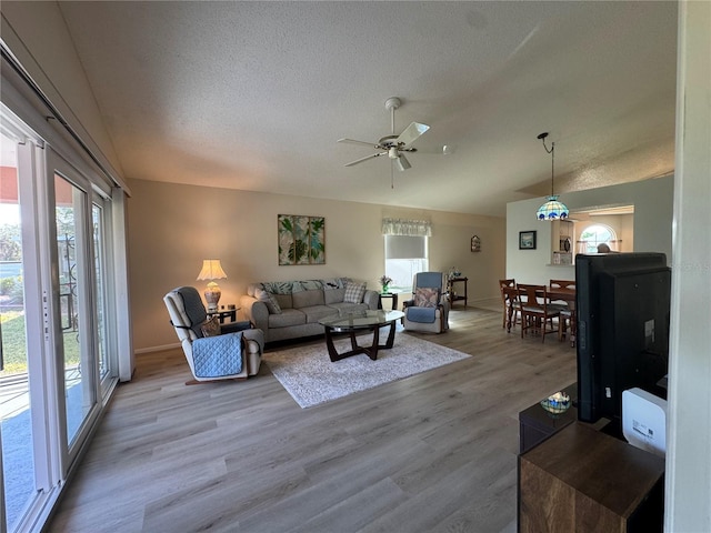 living area with baseboards, a ceiling fan, wood finished floors, vaulted ceiling, and a textured ceiling