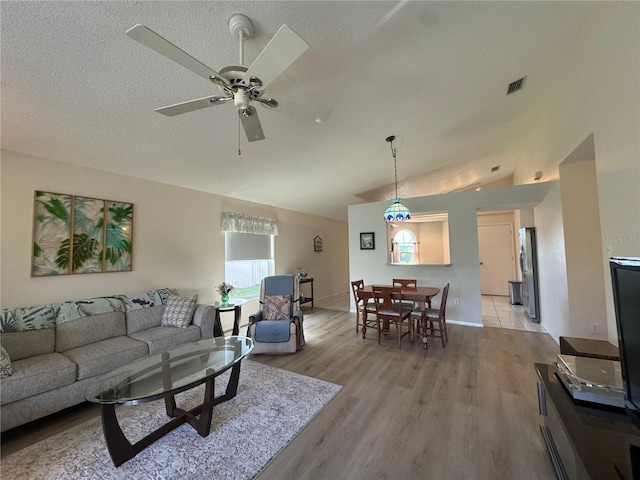 living room with visible vents, a ceiling fan, lofted ceiling, light wood-style flooring, and a textured ceiling