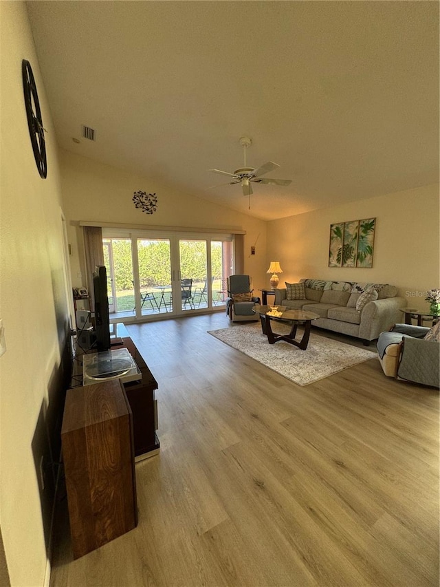 living area featuring a ceiling fan, visible vents, vaulted ceiling, and light wood finished floors