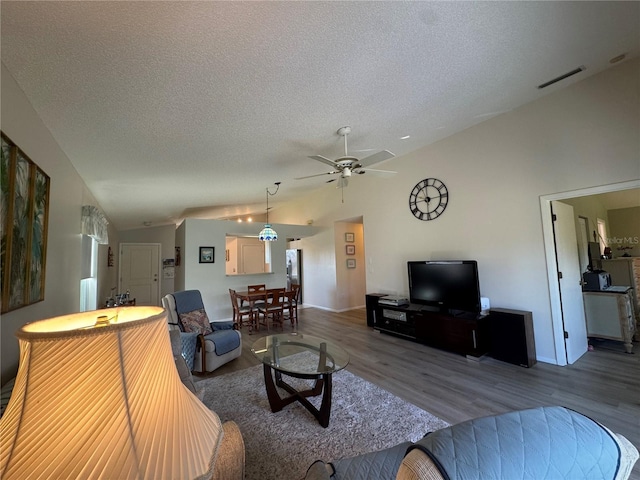 living area with visible vents, vaulted ceiling, a textured ceiling, and wood finished floors