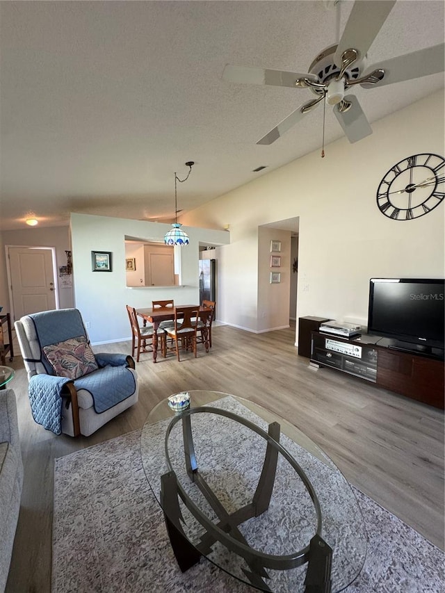 living room with lofted ceiling, light wood-style flooring, a ceiling fan, a textured ceiling, and baseboards