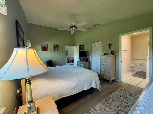 bedroom with light wood finished floors, visible vents, ensuite bath, vaulted ceiling, and a closet