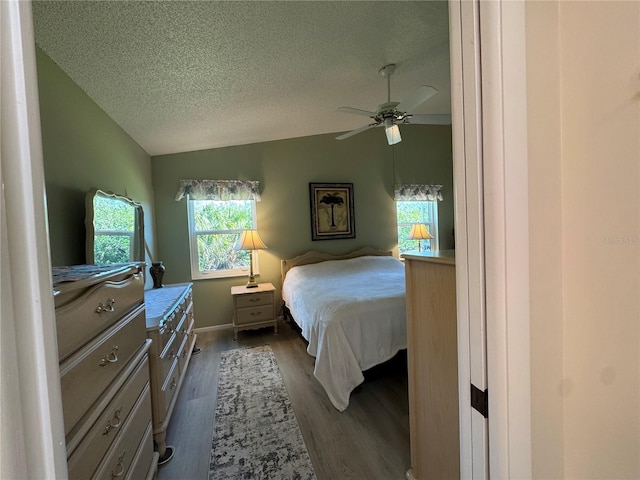 bedroom featuring lofted ceiling, a textured ceiling, dark wood-type flooring, a ceiling fan, and baseboards