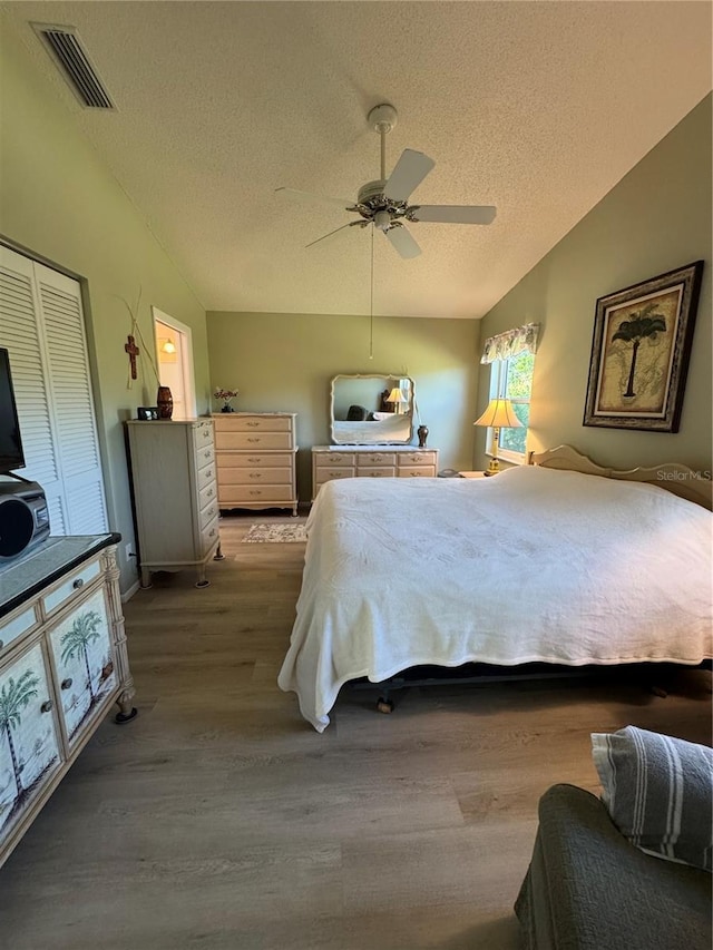 bedroom featuring visible vents, a ceiling fan, vaulted ceiling, a textured ceiling, and wood finished floors