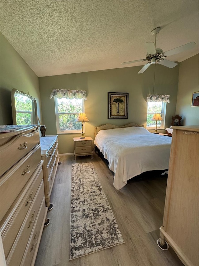 bedroom with lofted ceiling, light wood-style flooring, ceiling fan, and a textured ceiling