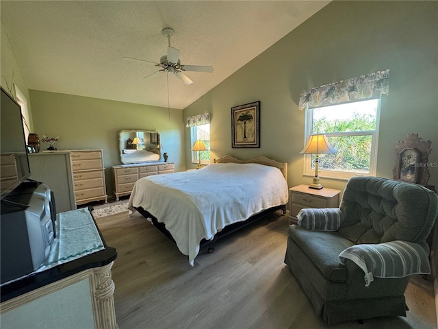 bedroom with lofted ceiling, light wood finished floors, a textured ceiling, and a ceiling fan