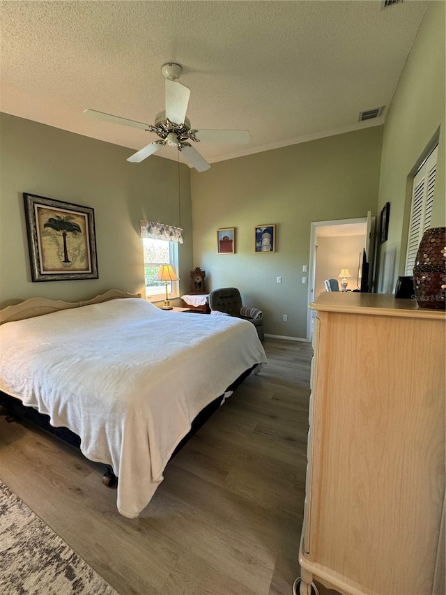 bedroom featuring dark wood-style floors, a ceiling fan, visible vents, and a textured ceiling