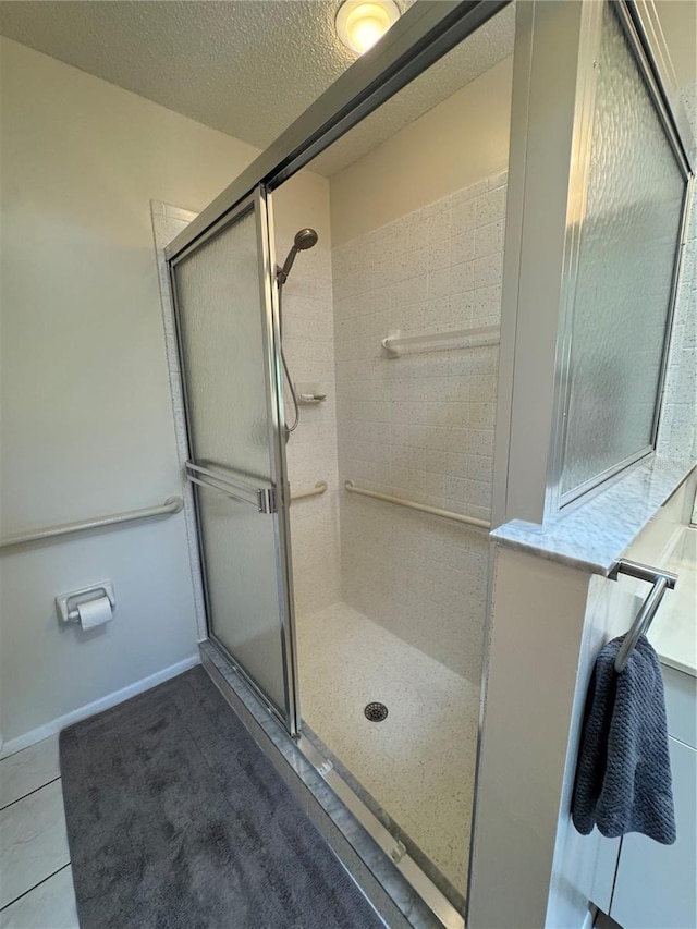 bathroom with tile patterned flooring, a tile shower, a textured ceiling, and baseboards