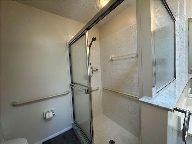 bathroom with baseboards, toilet, a textured ceiling, and a shower stall