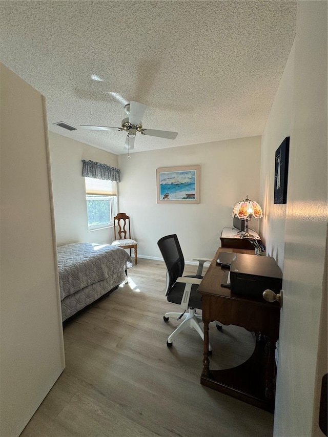 bedroom with a textured ceiling, light wood-type flooring, visible vents, and a ceiling fan