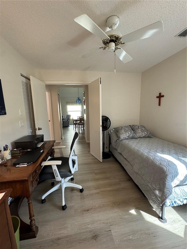 bedroom featuring a textured ceiling, a ceiling fan, visible vents, and light wood-style floors