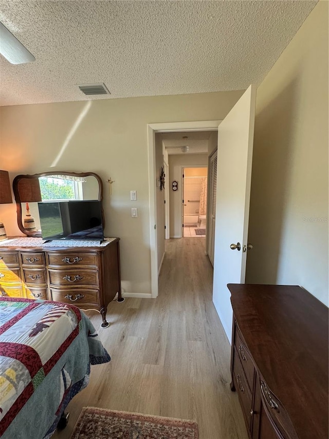 bedroom featuring light wood-type flooring, visible vents, a textured ceiling, and baseboards