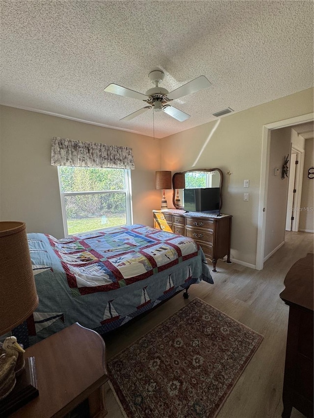 bedroom with visible vents, a ceiling fan, a textured ceiling, wood finished floors, and baseboards