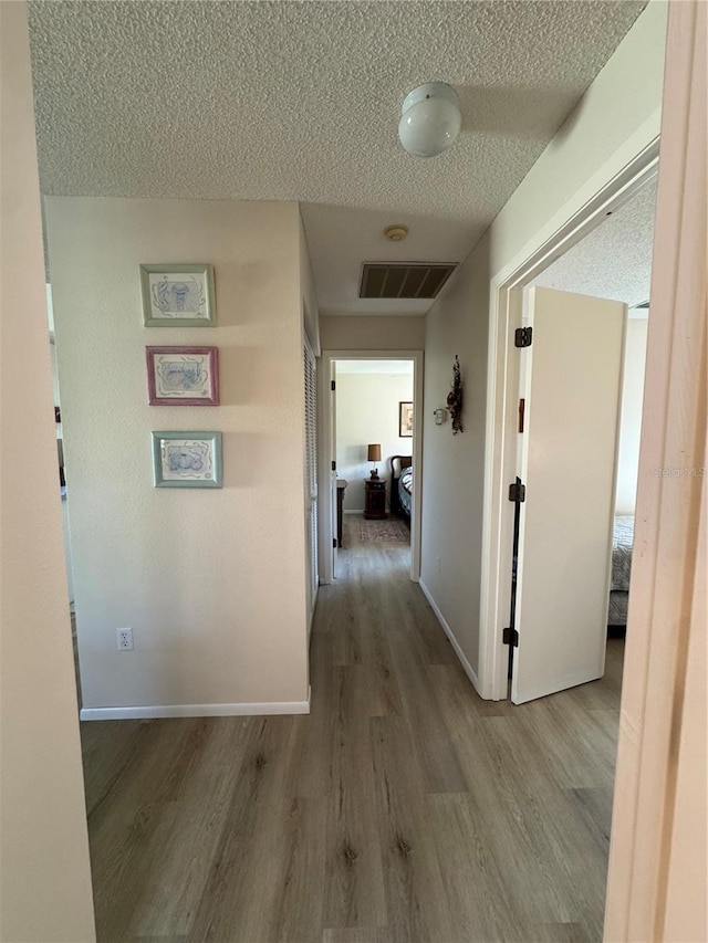 hallway featuring light wood-type flooring, visible vents, a textured ceiling, and baseboards