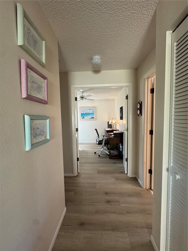 corridor featuring baseboards, light wood-style flooring, and a textured ceiling