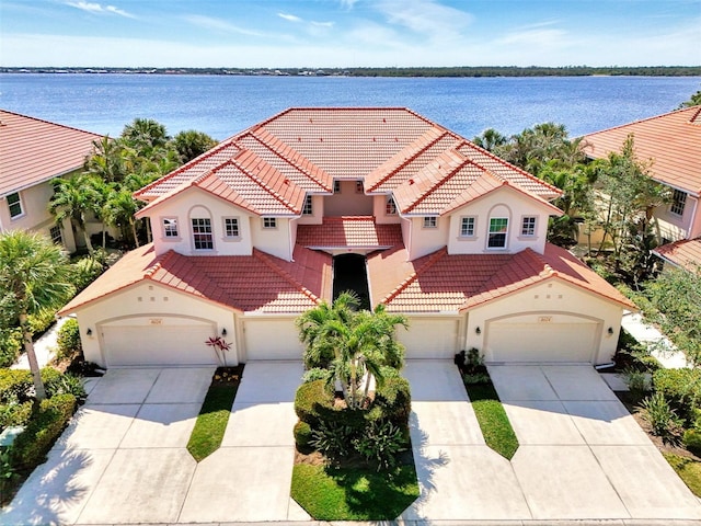 mediterranean / spanish home featuring a tile roof, a water view, driveway, and stucco siding