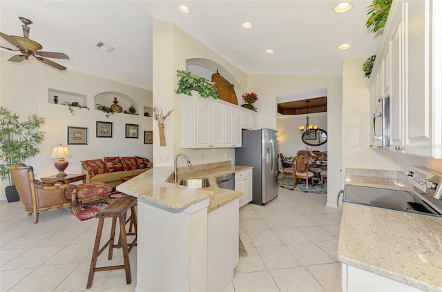 kitchen featuring light stone counters, stainless steel appliances, a peninsula, a sink, and white cabinetry