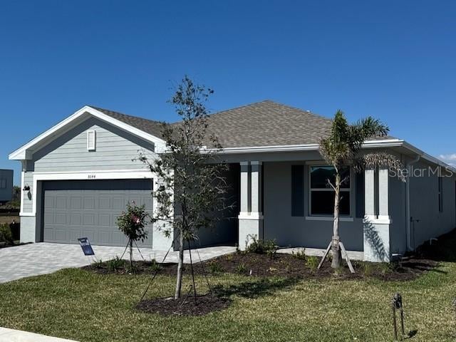 ranch-style house with a front yard, decorative driveway, roof with shingles, and an attached garage