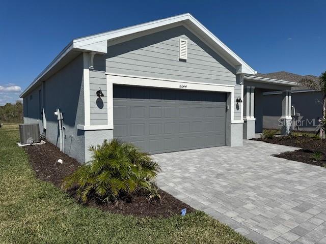 view of front of property with a garage, decorative driveway, stucco siding, and central air condition unit