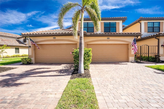 mediterranean / spanish-style house with a garage, a tile roof, decorative driveway, and stucco siding