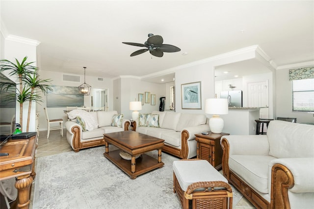 living room featuring light tile patterned floors, ceiling fan with notable chandelier, visible vents, and ornamental molding