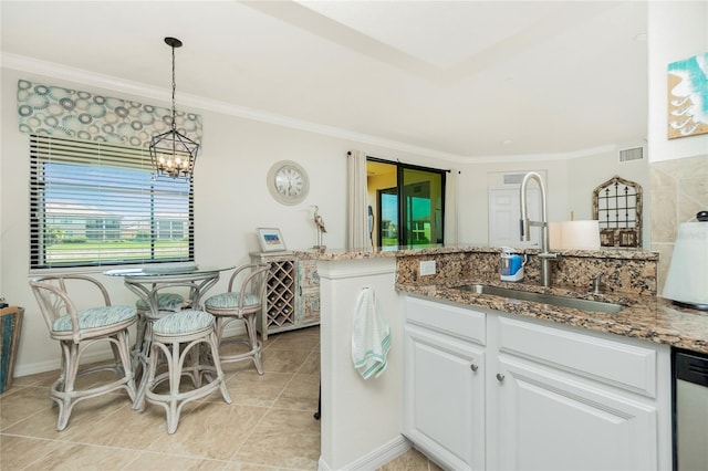 kitchen with light stone counters, a sink, visible vents, white cabinetry, and pendant lighting