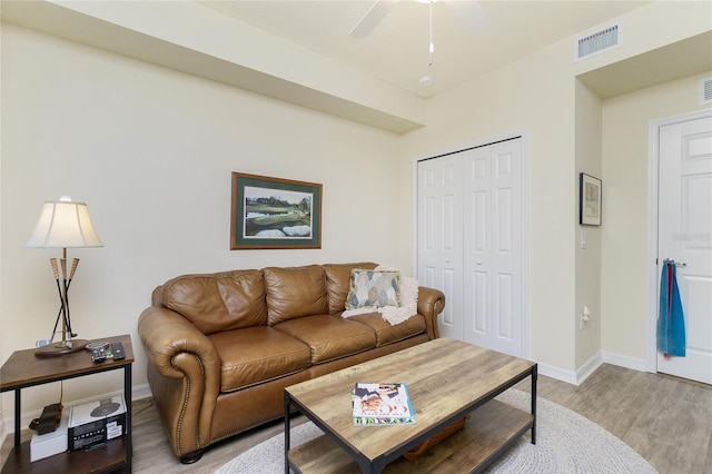 living room featuring light wood finished floors, a ceiling fan, visible vents, and baseboards