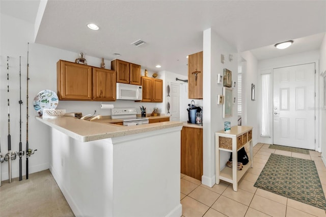 kitchen with a peninsula, white appliances, visible vents, light countertops, and brown cabinetry